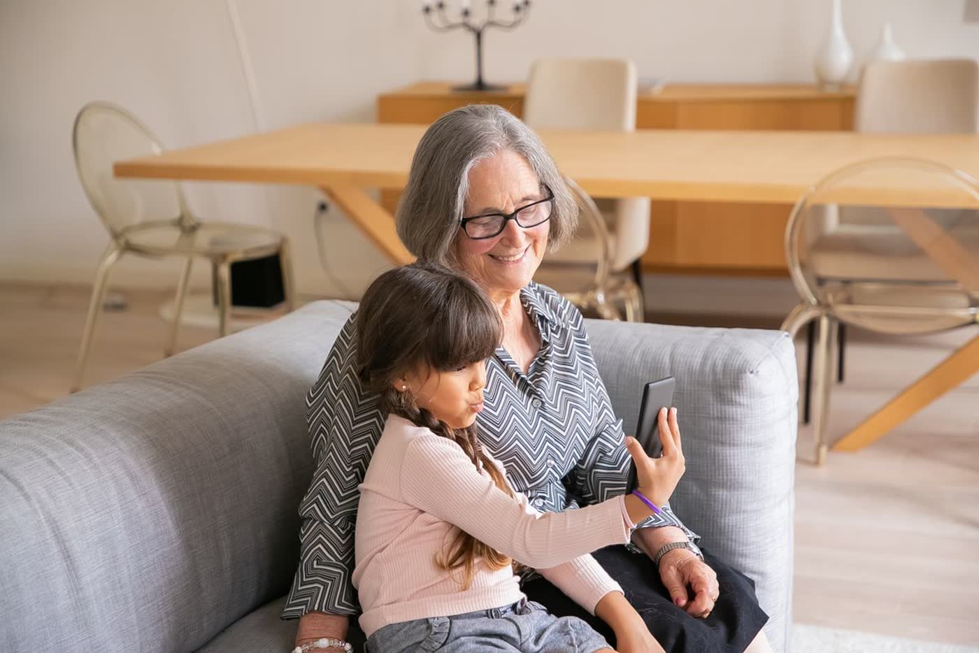 Una abuela y su nieta en el sofá de casa, mirando juntas un teléfono