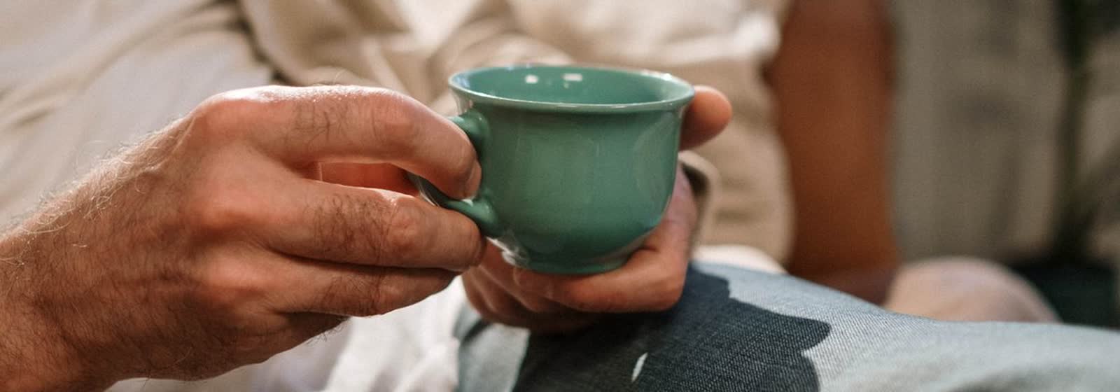 Unas manos sosteniendo una taza de cerámica en el sofá de casa