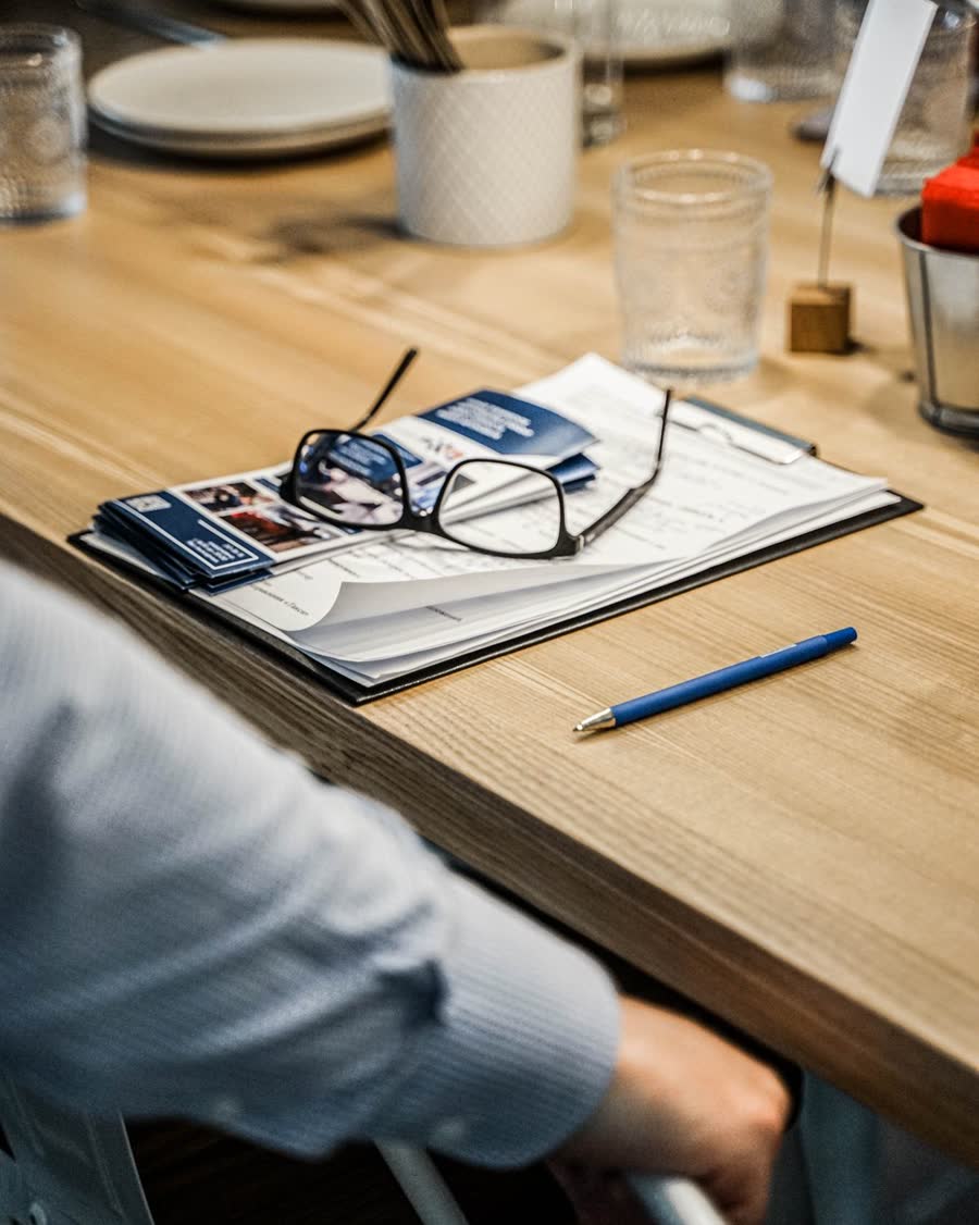 Papeles y una carpeta sobre una mesa de comedor de madera, con lentes encima